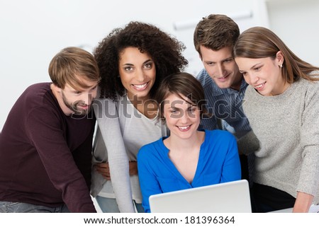 Multiethnic business team working in the office grouped around a laptop computer with an attractive African American woman looking up with a smile