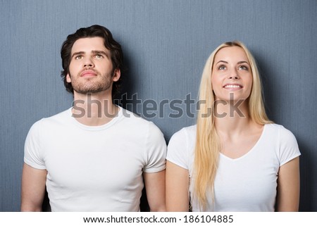 Attractive young couple standing side by side on a grey background thinking and looking up into the air
