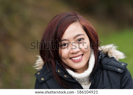 Attractive friendly young Asian woman standing outdoors in a polo neck sweater smiling at the camera
