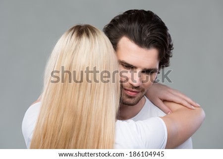 Young couple share a tender moment together as they hug each other tightly sharing their love, on grey