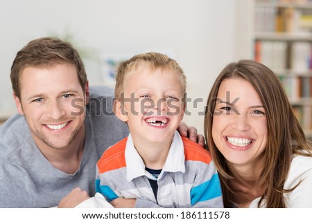 Adorable little boy with a happy grin and missing front teeth sitting between his laughing happy young parents in a beautiful loving family portrait