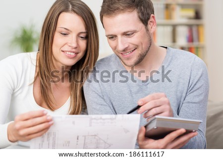 Young couple planning a new purchase sitting together pointing to a document held by the wife as the husband does the necessary calculations on a calculator