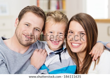 Beautiful happy young family posing together for a portrait with attractive young parents flanking a cute little boy with his front teeth missing