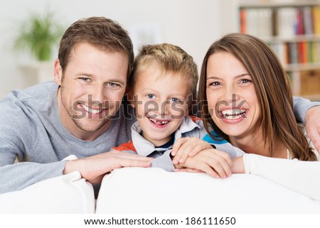 Laughing happy young family posing together in the living room with an adorable young boy with missing front teeth flanked by his attractive smiling parents