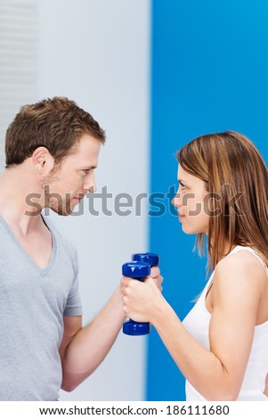 Competitive young couple working out at the gym facing off staring at each other as they work out with dumbbells in a health and fitness concept