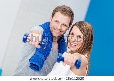 Playful happy happy couple working out together in a gym with dumbbells laughing as they extend them towards the camera in a health and fitness concept