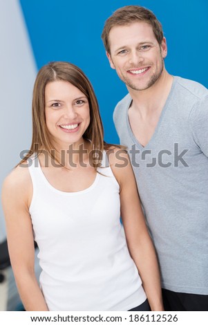 Smiling friendly fit young couple posing side by side looking at the camera with warm friendly smiles