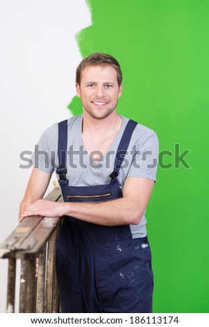 Smiling handyman or homeowner carrying a wooden stepladder as he paints the house during a redecorating project