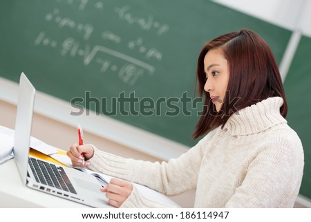 Beautiful young Asian student hard at work sitting at her desk in the classroom using a laptop computer, side view