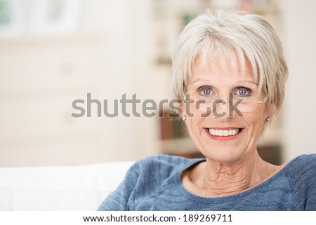 Happy attractive grey-haired senior woman with a beautiful smile relaxing at home on a sofa looking at the camera with copyspace alongside