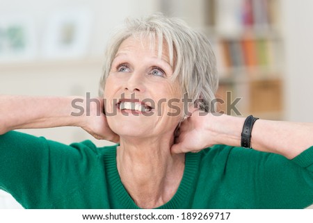 Beautiful elderly lady with a radiant smile sitting with her hands clasped behind her head daydreaming as she stares up into the air