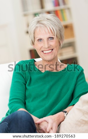 Confident relaxed beautiful senior woman sitting on a sofa at home giving the camera a lovely warm smile