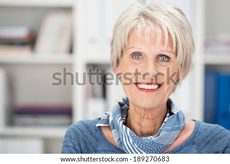 Happy senior woman with beautiful blue eyes wearing a stylish scarf standing in an office smiling at the camera
