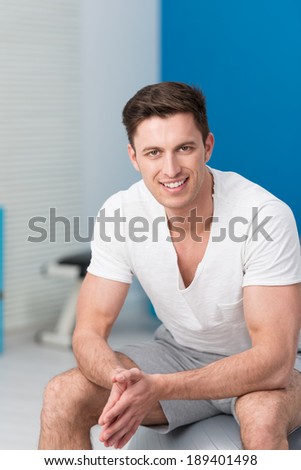 Athletic young man sitting on a pilates ball at the gym looking at the camera with a friendly smile