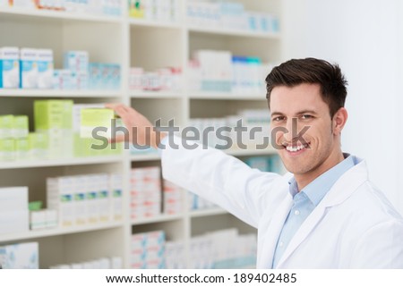 Smiling handsome male pharmacist promoting a product holding it in his hand visible to the camera with a friendly smile