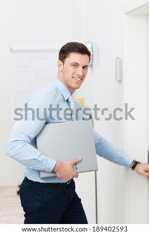 Busy young businessman leaving the office with a folder under his arm reaching out to open the door
