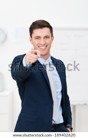 Handsome young businessman pointing at the camera with a beaming smile as he makes a choice, presentation or identifies someone