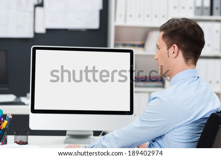 Businessman working at his desk with the blank screen of his desktop computer visible to the viewer