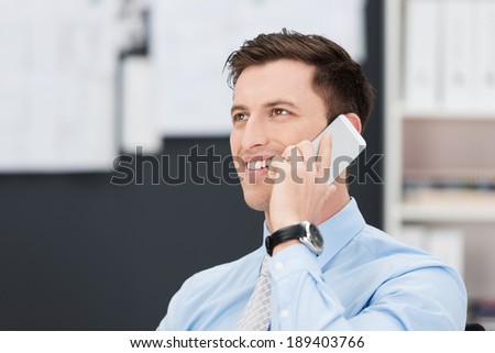 Handsome businessman talking on his mobile phone listening to the conversation with a smile as he sits in the office