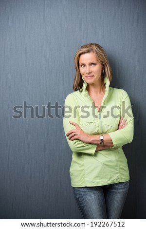 Confident relaxed trendy middle-aged woman leaning against a grey background with folded arms smiling at the camera