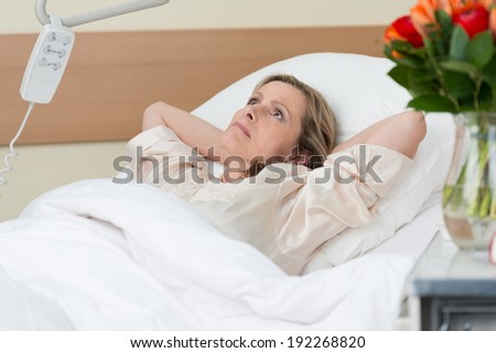 Worried middle-aged woman lying thinking in a hospital bed with her hands clasped behind her head as she stares at the ceiling with an intense expression