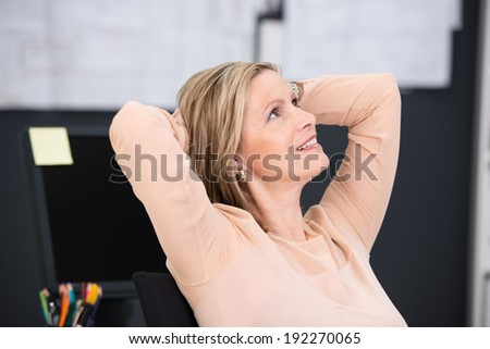 Smiling businesswoman sitting daydreaming as she relaxes at the offices sitting back in her chair with her hands clasped behind her head
