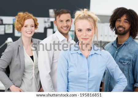 Successful confident young multiethnic business team led by an attractive young blond woman smiling happily as they pose for the camera