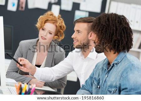 Three diverse multiethnic young business colleagues in a meeting discussing information on a computer monitor