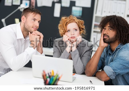 Young business team at a loss for a solution sitting at a table with serous expression deep in contemplation as they seek an answer
