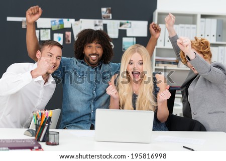 Young multiethnic business team cheering as they sit grouped around a laptop computer celebrating a success