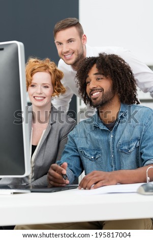 Happy African American man at work smiling as he sits with his colleagues in the studio at a computer creating a new innovation or design