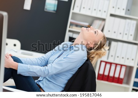 Smiling happy businesswoman sitting daydreaming leaning back in her chair with her head tilted back smiling up at the ceiling