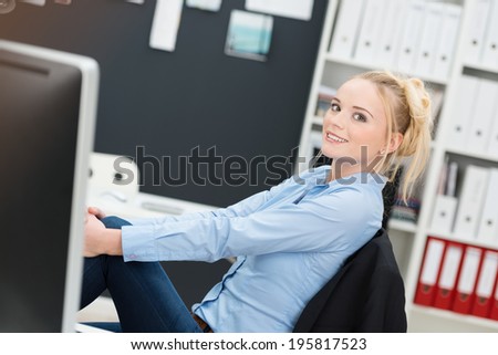 Young businesswoman relaxing at her desk sitting back in her chair at the office with her feet up smiling at the camera