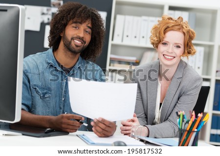 Happy multiethnic business partners sitting together in the office with a casual young African American man and beautiful redhead woman discussing a document