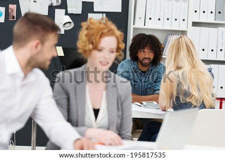 Busy day at the office with a selective focus image of two businesspeople having a discussion at the back of the office while a young man and woman work in the foreground