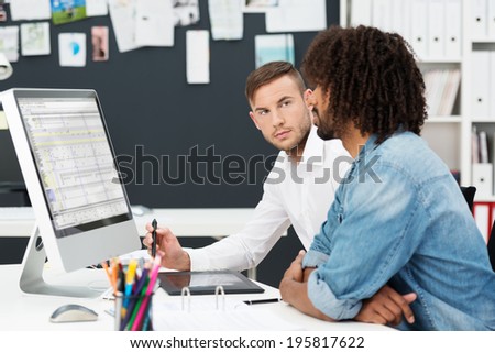 Two young men having a business meeting with an African American sitting looking at information on the computer watched closely by his colleague