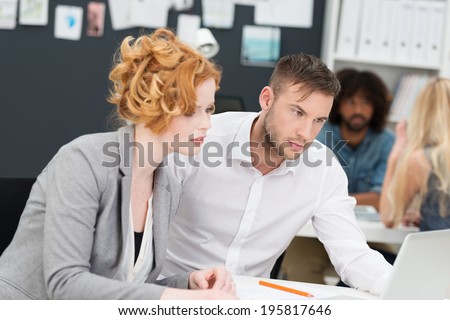 Two concerned young business people, an attractive woman and man, staring at a laptop computer with worried frowns as they sit working at a desk together