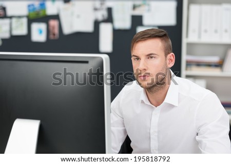 Handsome young businessman concentrating on his work as he reads information on a large desktop monitor