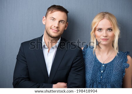 Attractive young couple posing side by side facing the camera with a smile standing against a grey studio background