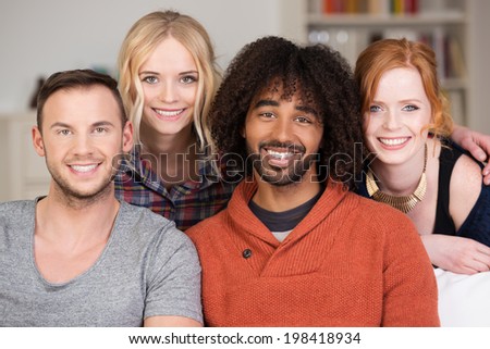 Relaxed group of four young multiracial friends posing together on a couch in the living room smiling happily at the camera