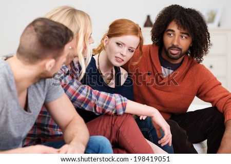 Group of multiracial young friends having a serious discussion sitting in a row on a couch leaning forwards to communicate better
