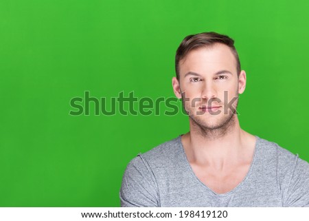 Handsome young man with a stubble beard standing against a green background with copyspace giving the camera an intense serious stare