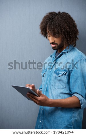 Young African American student standing working on his tablet computer against a blank chalkboard