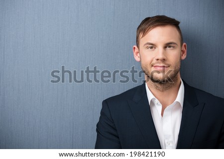 Friendly young unshaven businessman in an open necked shirt and jacket posing in front of a grey background with copyspace