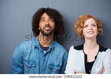 Young attractive multiethnic couple smiling as they stand daydreaming and planning for the future, against a grey background