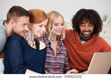 Group of four young multiracial friends smiling as they surf the internet together on a tablet computer while spending a relaxing day at home