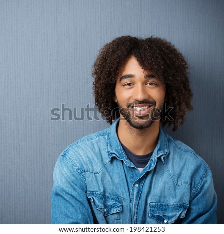 Happy young African American man with a big friendly smile and curly afro hairdo, upper body against a grey studio background