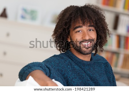 Happy young African American man with a lovely smile and wild curly afro hairstyle relaxing at home in his living room, head and shoulders portrait
