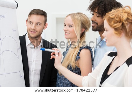 Young multiethnic business team planning a new strategy standing grouped in front of a flip chart analyzing a chart