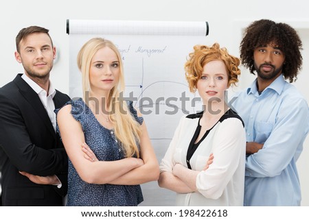 Serious young group of business men and women standing facing the camera with folded arms in front of a flip chart